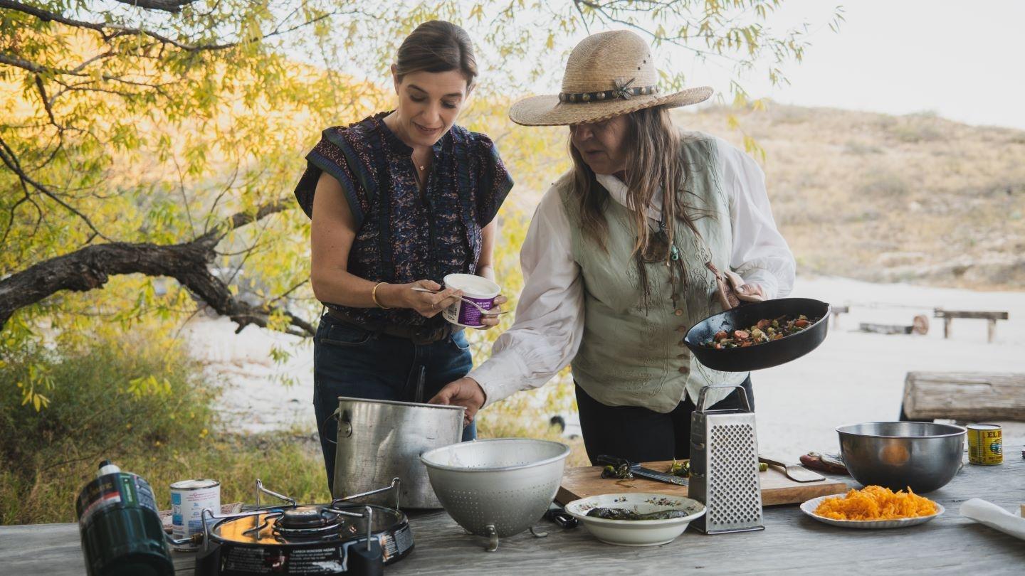 Two women are shown cooking at a table outdoors.